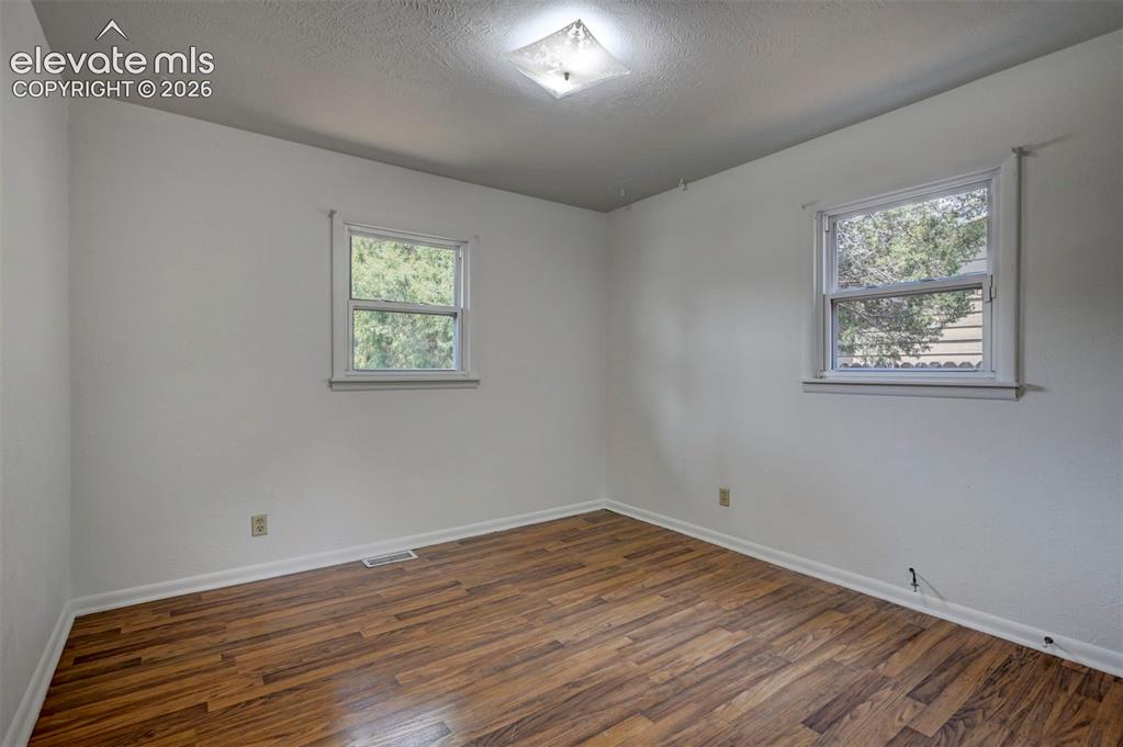 Image 27 of 40: Room featuring wood-finish flooring, white baseboards, and two windows with