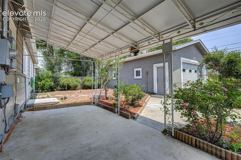 Image 31 of 40: Covered concrete patio with a detached garage featuring a white overhead do