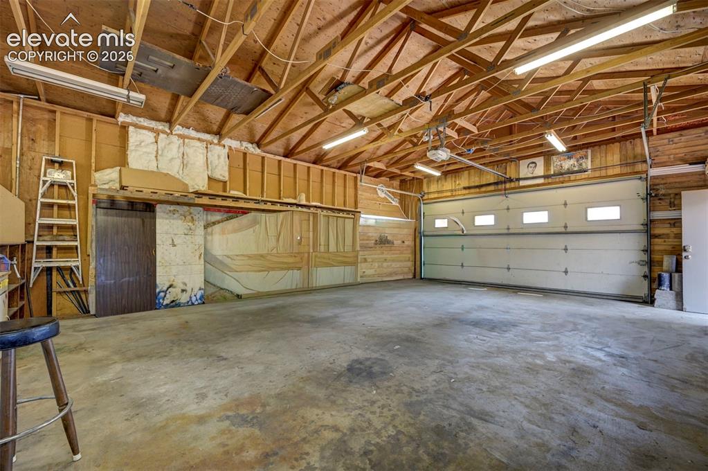 Image 39 of 40: Spacious garage featuring a concrete floor, exposed wood beam ceiling, and