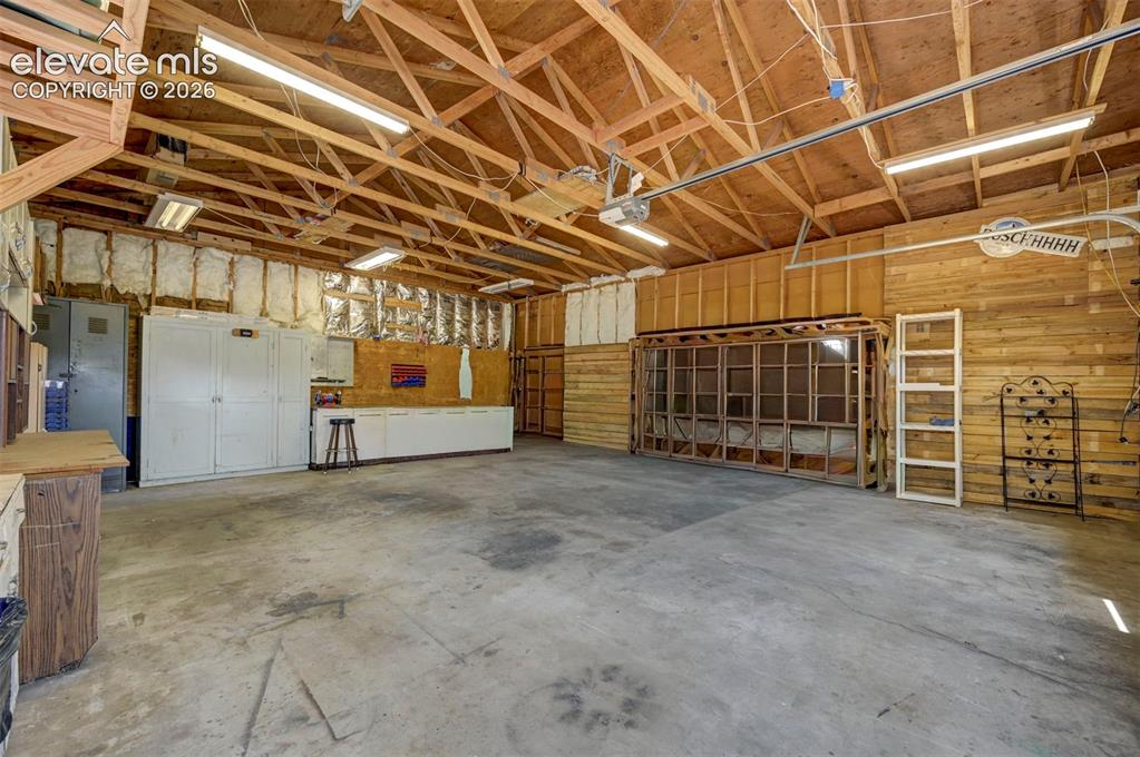 Image 40 of 40: Spacious garage featuring a concrete floor, exposed wood beam ceiling, and