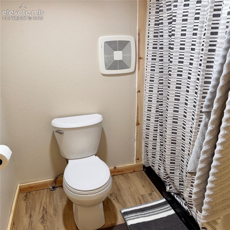 Image 18 of 45: Wood-finish flooring with a white toilet and an exhaust fan