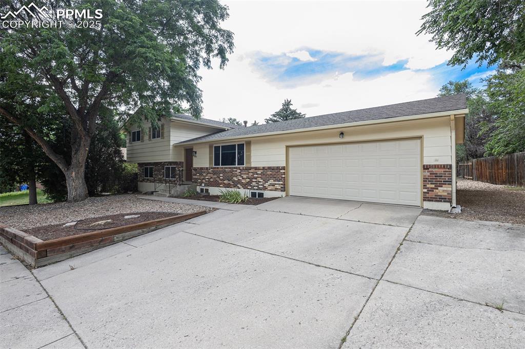Image 2 of 29: Split level home with brick siding, driveway, a garage, and roof with shing