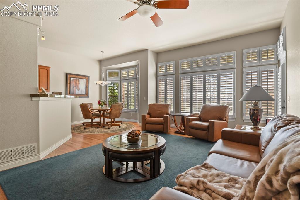 Image 12 of 46: Bright living area featuring a ceiling fan, bay windows with plantations sh