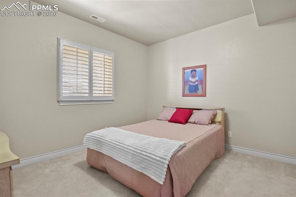 Image 31 of 46: Third bedroom features a window with white plantation shutters and carpetin