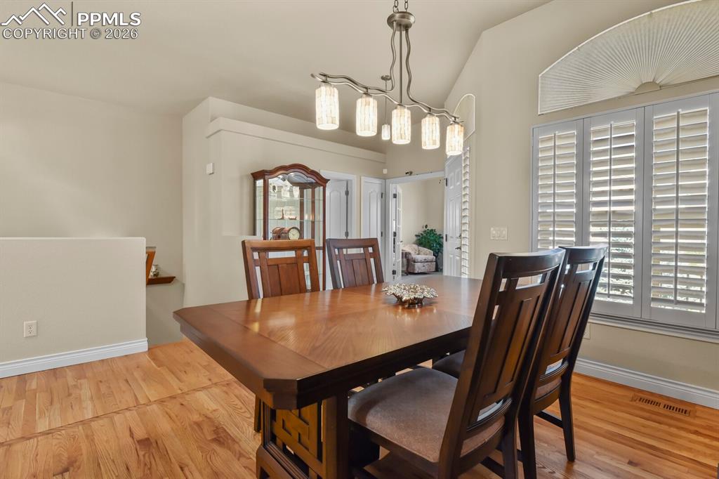 Image 6 of 46: Dining area featuring hardwood floors, a vaulted ceiling, and a decorative 