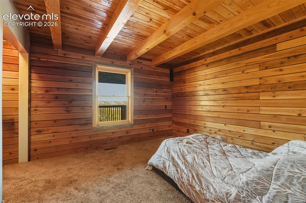 Image 11 of 40: Wood-paneled walls, exposed wood beam ceiling, single window, and neutral c