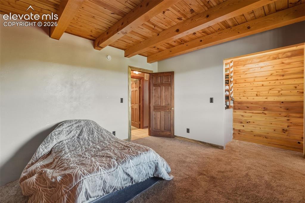 Image 12 of 40: Exposed wood beam ceiling, wood plank wall accent, wood-finish door, and ne