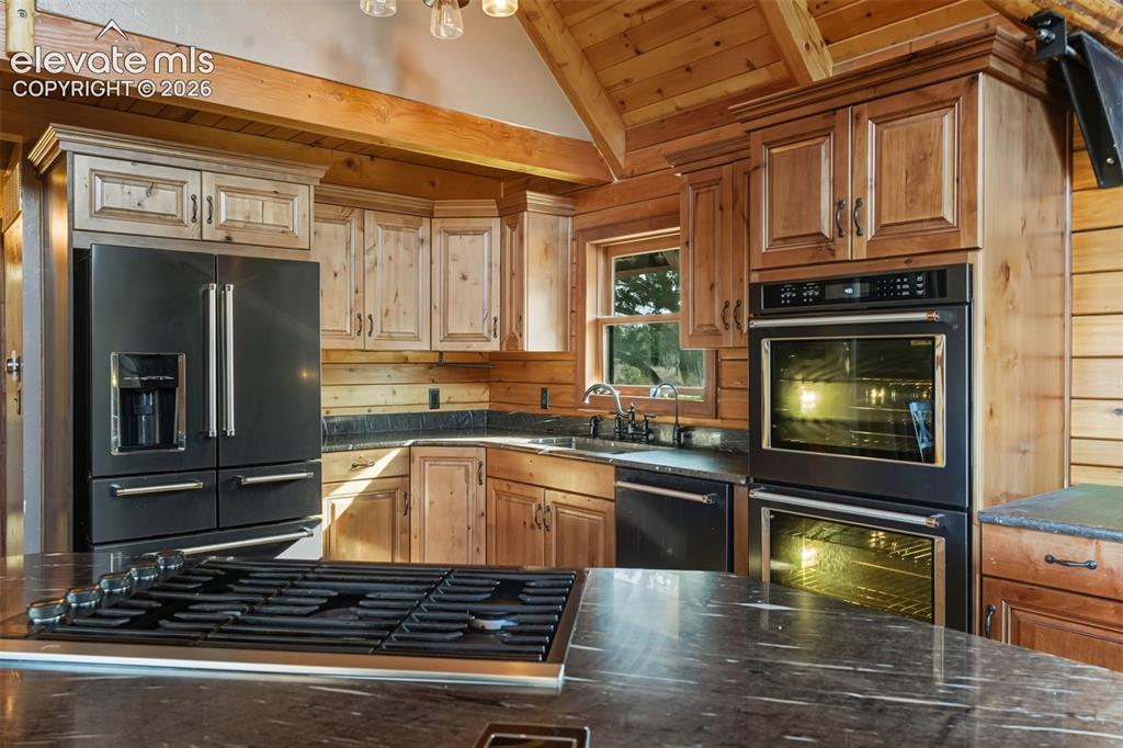 Image 21 of 43: Exposed wood beam ceiling, knotty pine cabinetry, integrated double wall ov