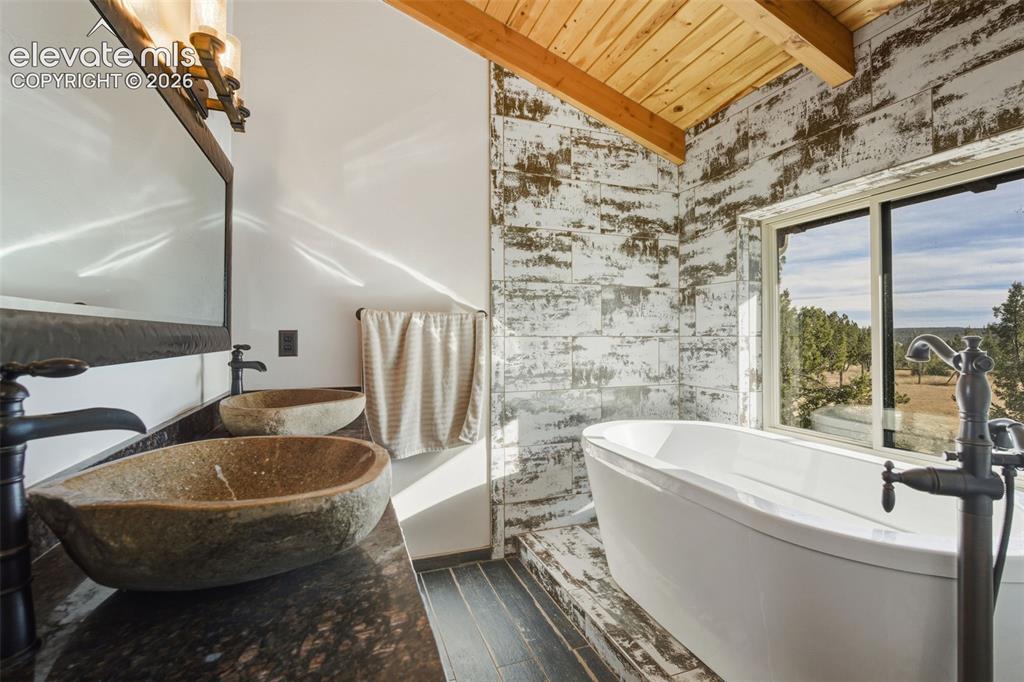 Image 30 of 43: Double basin vanity with stone vessel sinks, freestanding soaking tub, wood