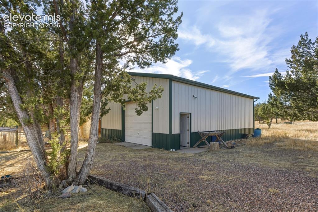 Image 31 of 40: Metal structure with a rolling garage door, pedestrian door, and a gravel s