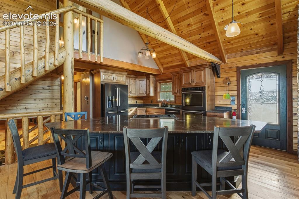 Image 9 of 40: Vaulted wood-paneled ceiling with exposed beams, wood-finish flooring, kitc