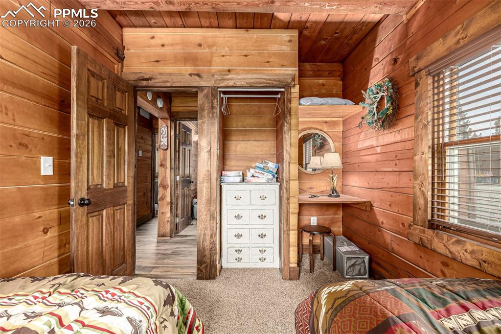 Image 29 of 35: Bedroom with wooden walls, wooden ceiling, and carpet floors
