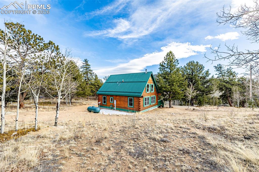 Image 33 of 35: Back of property featuring metal roof, log exterior, and view of wooded are
