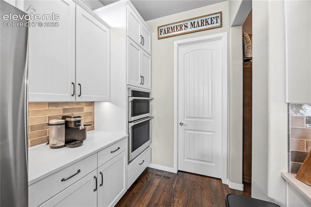 Image 11 of 50: Kitchen featuring white cabinetry, integrated double ovens, and a subway ti