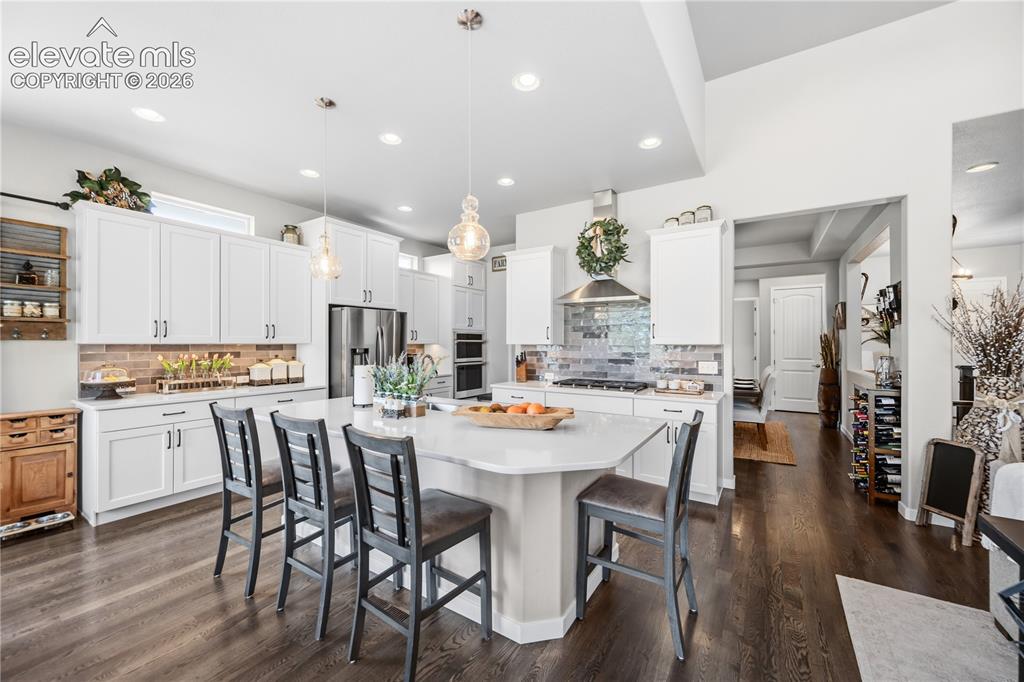 Image 12 of 50: Bright kitchen featuring a large central island with seating, white shaker