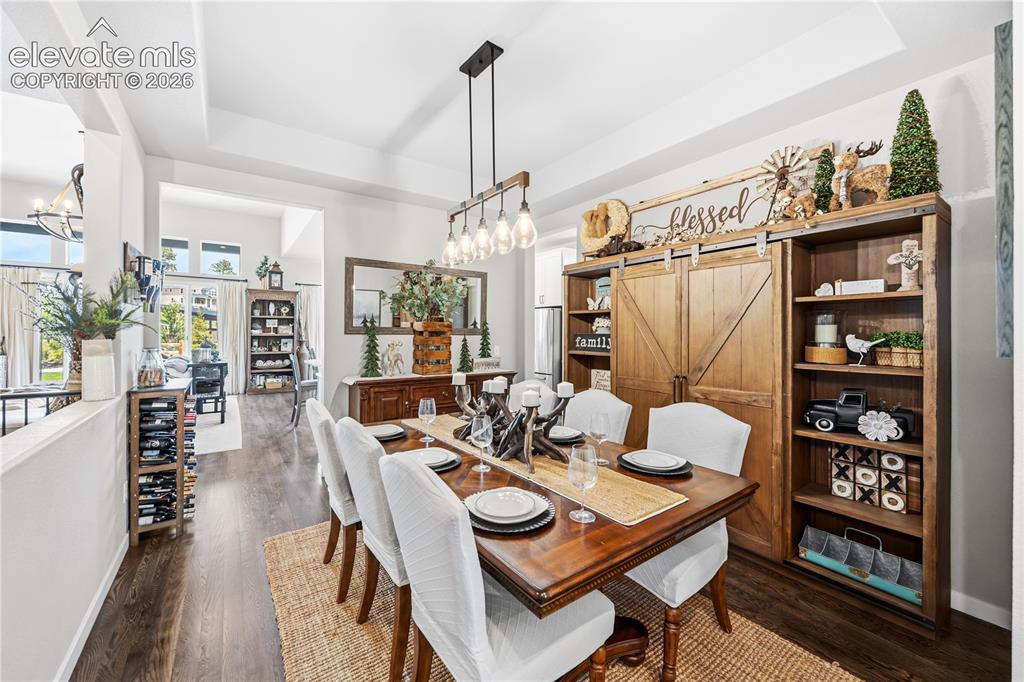 Image 13 of 50: Dining area featuring wood-finish flooring, a tray ceiling, and a prominent