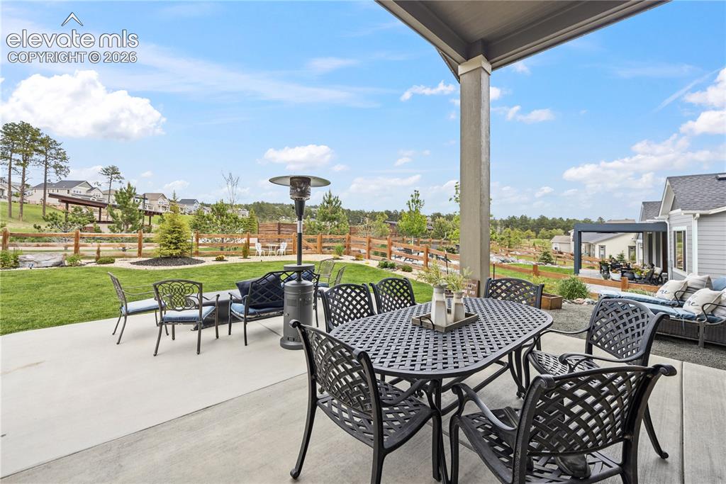 Image 14 of 50: Covered concrete patio with a structured overhead beam, bordered by a woode