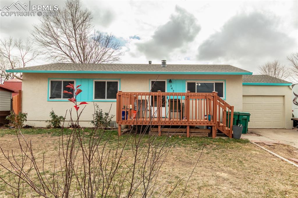 Caption: View of front facade featuring a shingled roof, a deck, stucco siding, and a front lawn