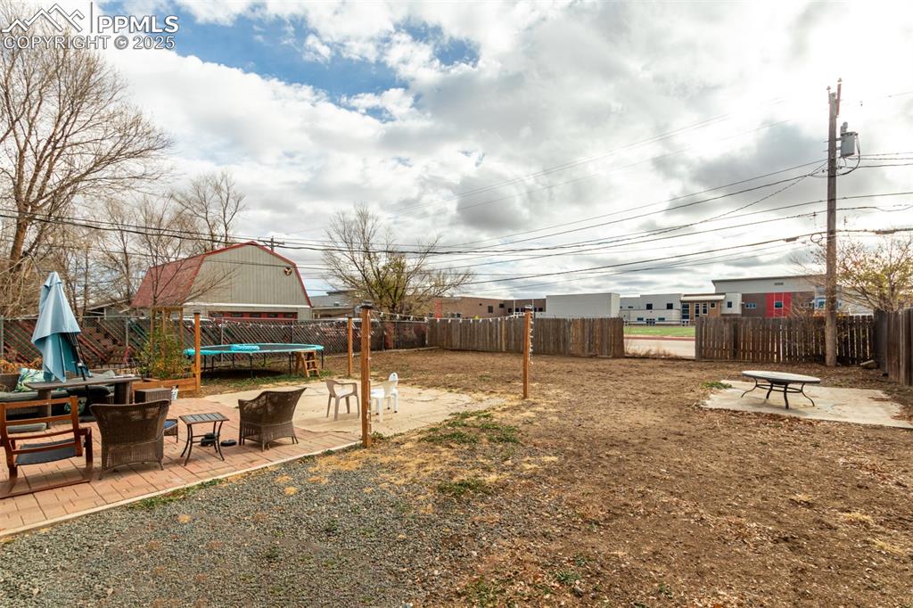 Image 13 of 17: Fenced backyard with a patio area, a trampoline, and a fire pit