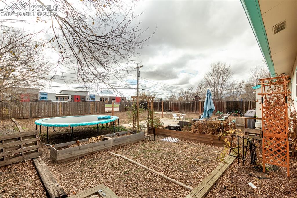Image 14 of 17: Fenced backyard featuring a garden, a trampoline, and a wooden deck