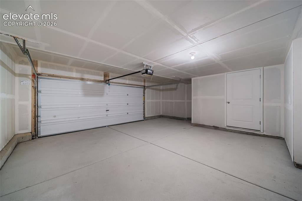 Image 6 of 26: Attached garage featuring a sectional overhead door, concrete flooring, and