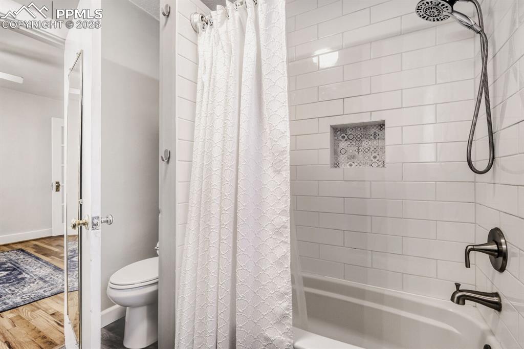Image 16 of 34: Bathroom with shower / tub combo with curtain and wood finished floors
