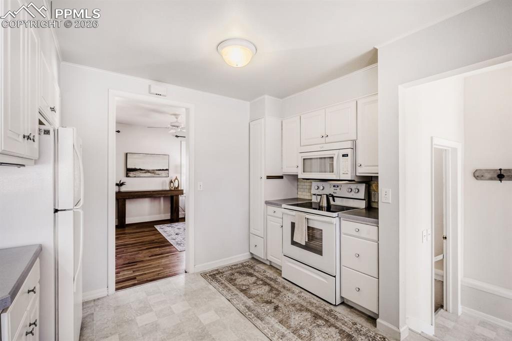 Image 7 of 34: Kitchen featuring white appliances, white cabinets, and backsplash