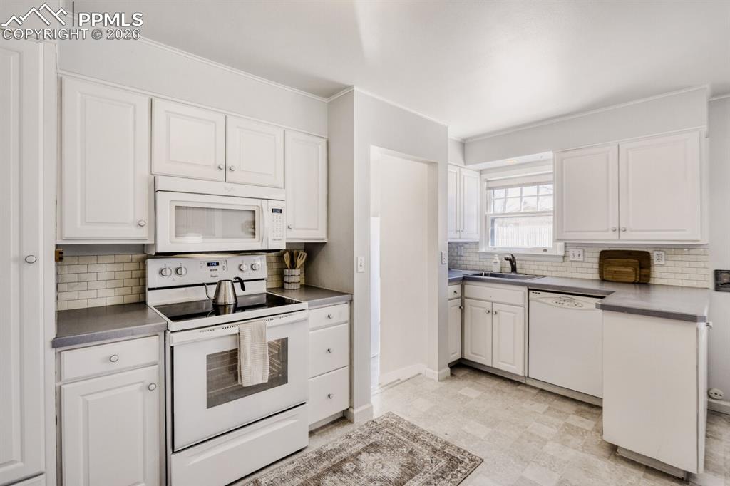 Image 8 of 34: Kitchen featuring white appliances, white cabinets, backsplash, ornamental 