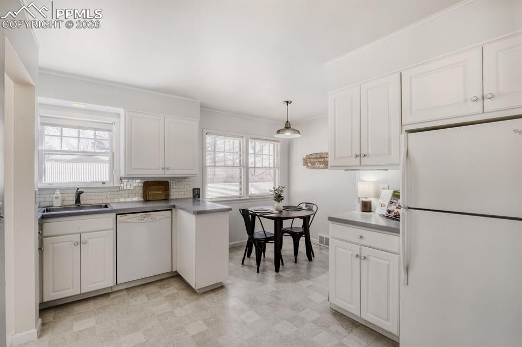 Image 9 of 34: Kitchen featuring white appliances, white cabinetry, hanging light fixtures