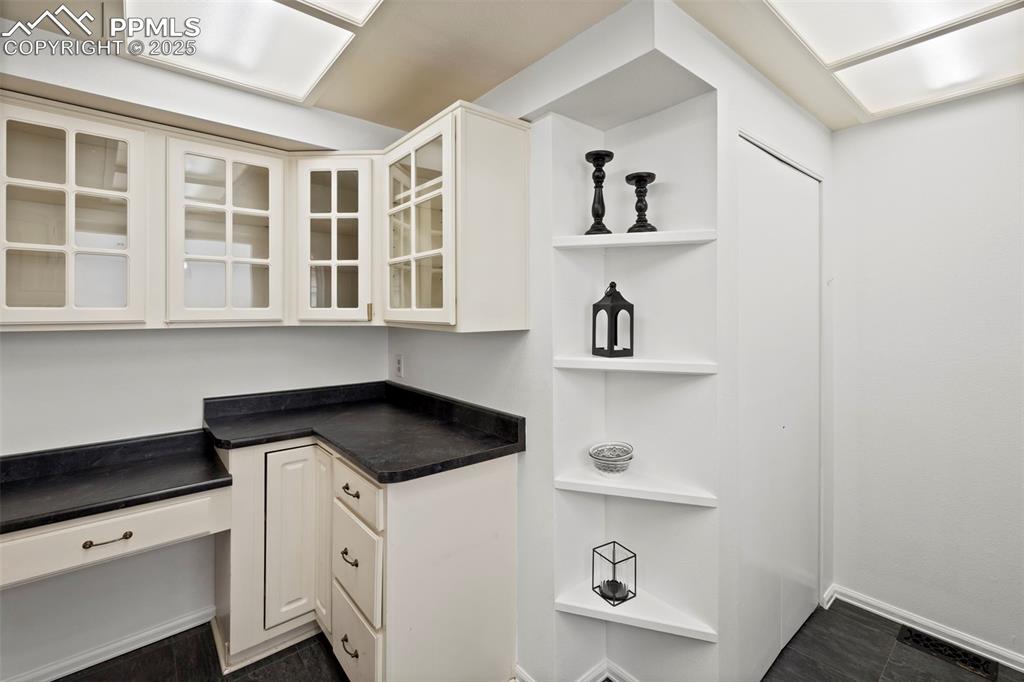 Image 12 of 31: Kitchen with dark countertops, white cabinetry, open shelves, and glass ins