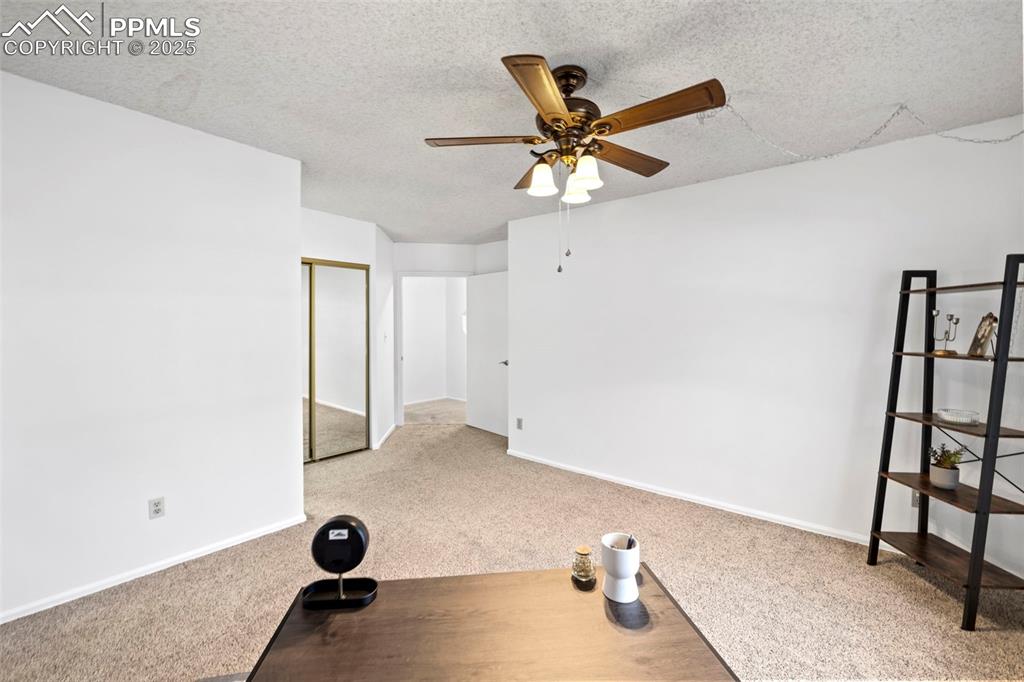 Image 20 of 31: Exercise area with light colored carpet, a textured ceiling, and ceiling fa