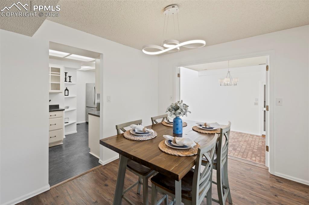Image 6 of 31: Dining space with a textured ceiling, dark wood-style flooring, and a chand
