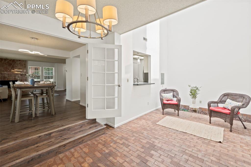 Image 8 of 31: Sitting room with a textured ceiling, brick patterned flooring, a chandelie
