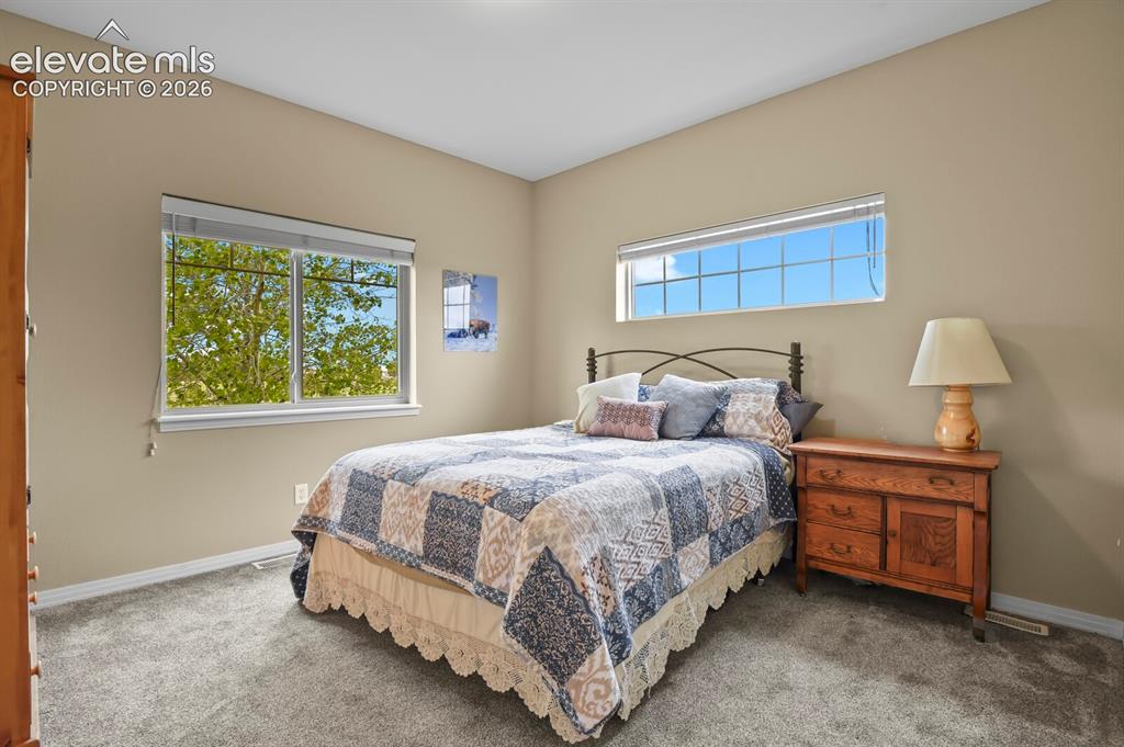Image 19 of 45: Bright secondary bedroom with large windows, neutral finishes, and comforta