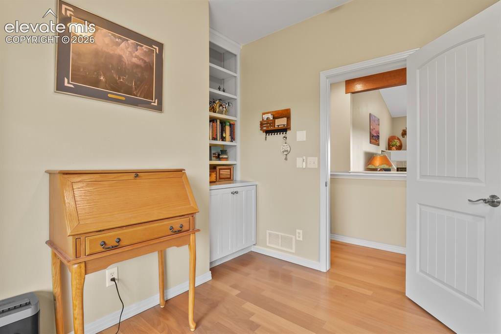 Image 23 of 45: Dedicated office/den featuring built-in shelving, hardwood flooring, and co