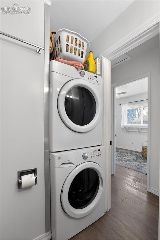 Image 16 of 19: Dedicated laundry area featuring stacked appliances and wood-finish floorin