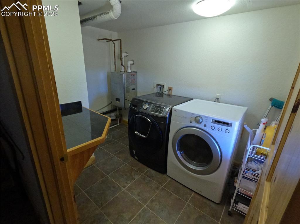 Image 15 of 23: Laundry area featuring dark tile patterned floors, washing machine and clot