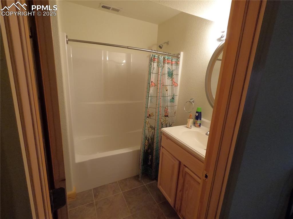 Image 17 of 23: Bathroom with dark tile patterned floors, vanity, shower / bath combo, and 