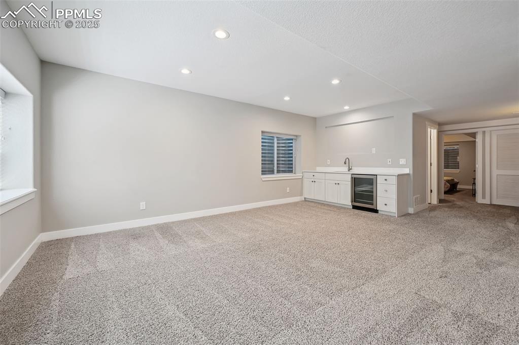 Image 31 of 39: Unfurnished family room featuring light carpet, beverage cooler, recessed l