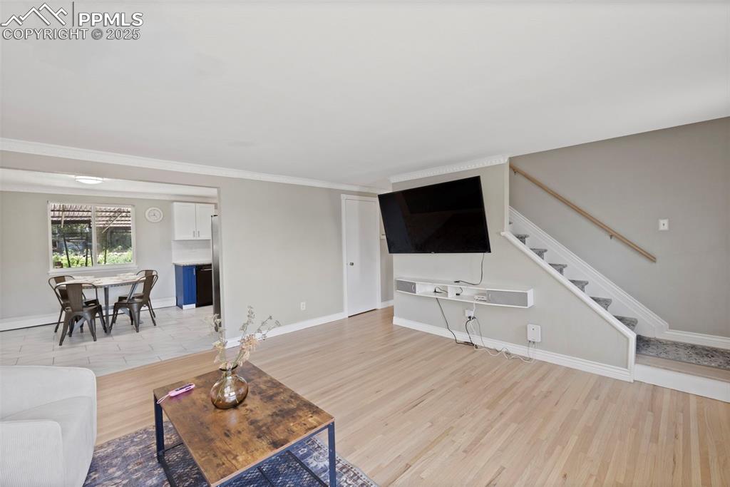 Image 2 of 33: Living area with light wood-type flooring, stairway, and ornamental molding