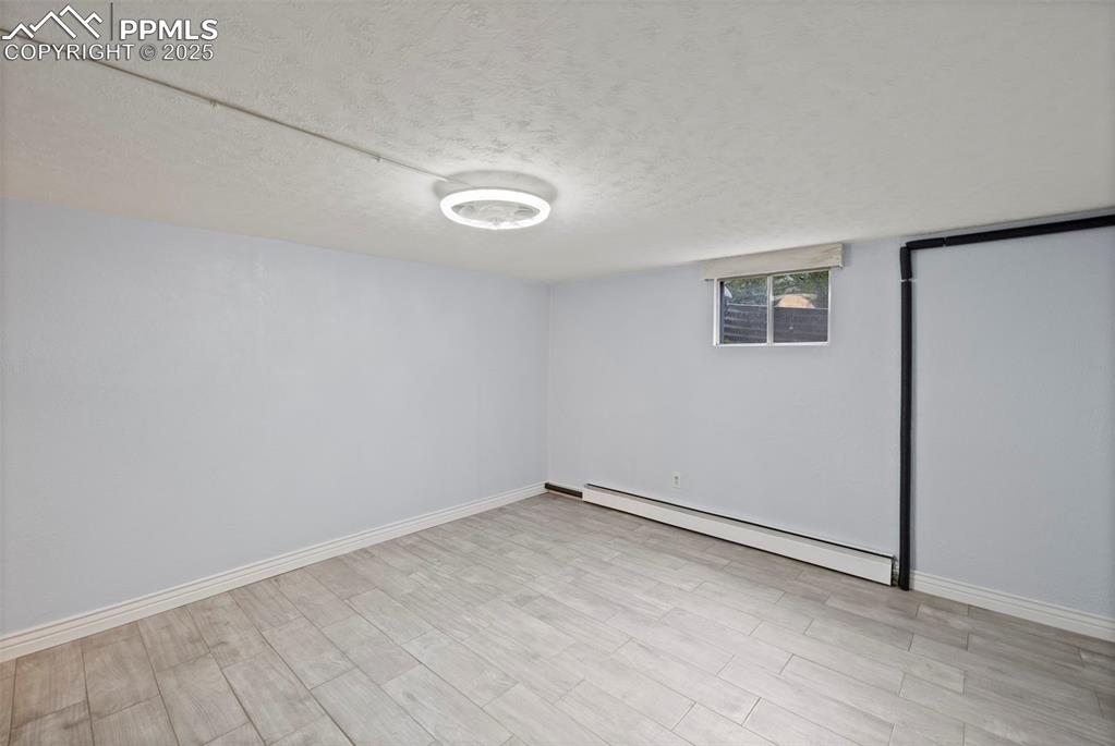 Image 22 of 33: Basement featuring a textured ceiling, a baseboard heating unit, and wood f