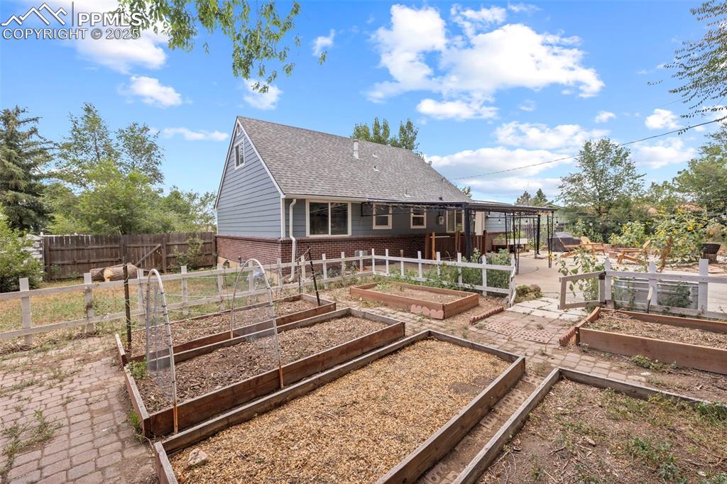Image 31 of 33: Rear view of house with a vegetable garden, brick siding, and roof with shi