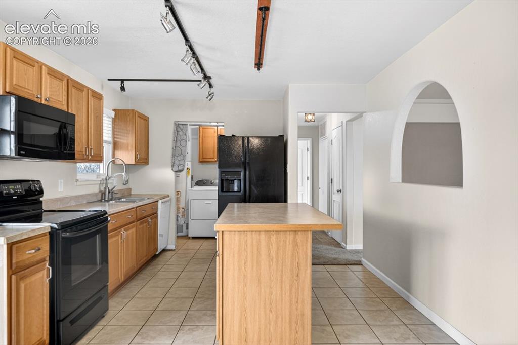 Image 10 of 25: Kitchen featuring wood cabinetry, black appliances, track lighting, a centr