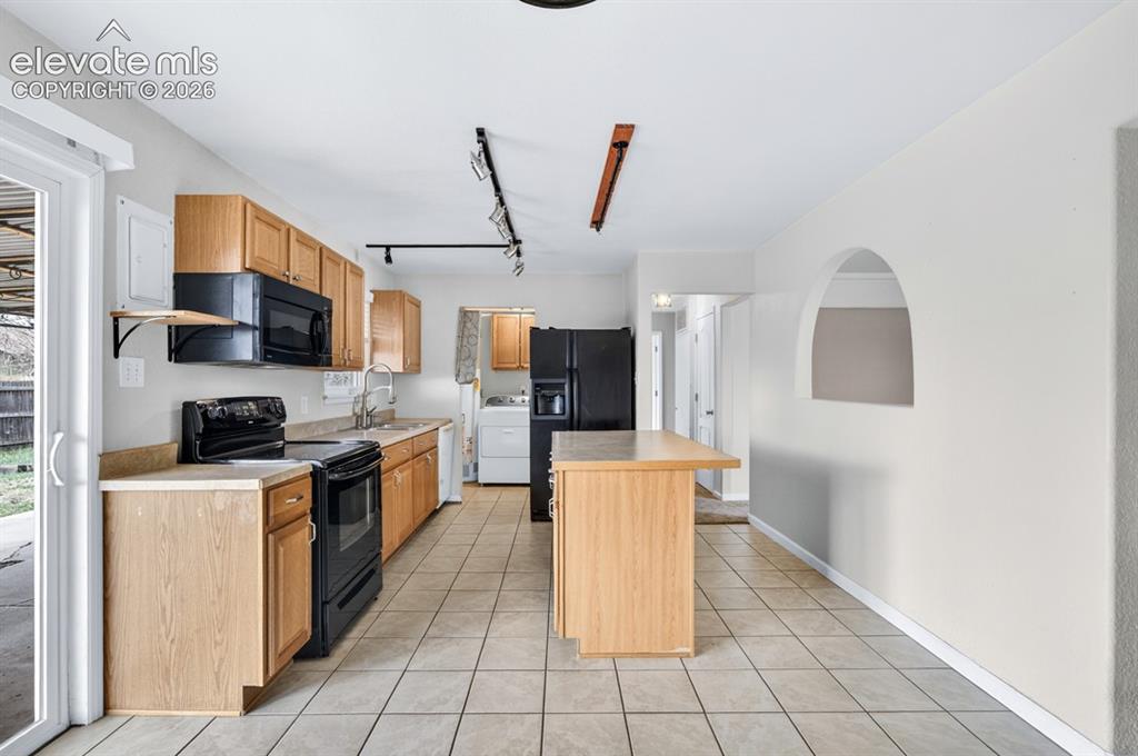 Image 11 of 25: Kitchen with wood cabinetry, black appliances, tile flooring, and a center