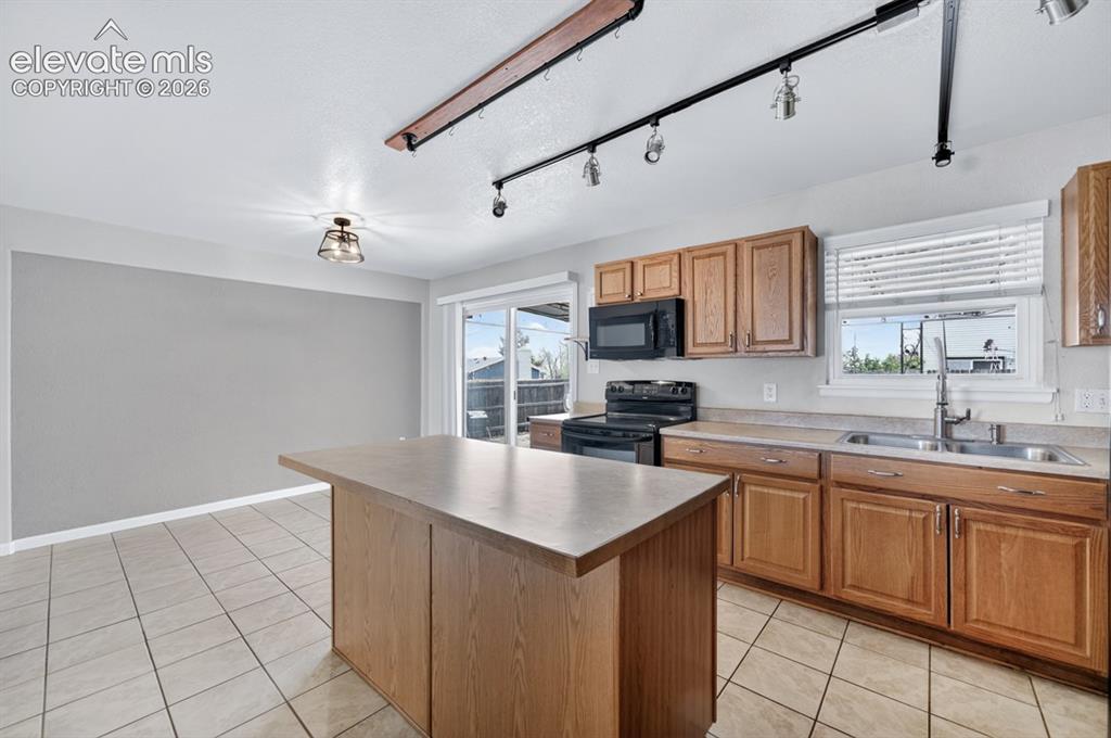 Image 12 of 25: Kitchen featuring a central island, wood-finish cabinetry, tile flooring, a