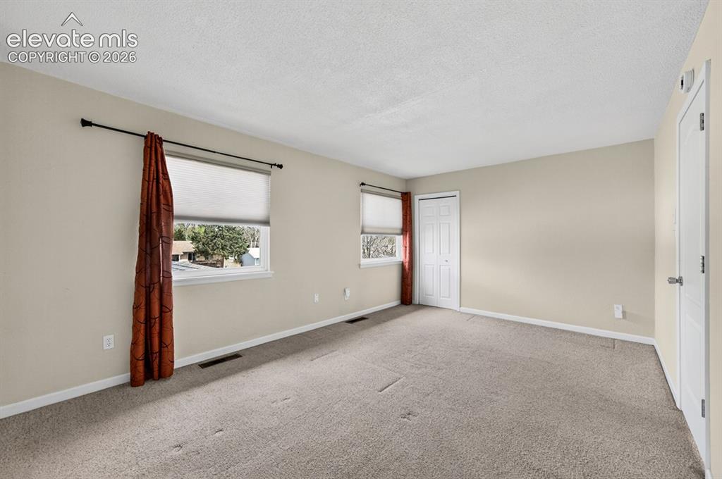 Image 13 of 25: Neutral wall tones, two windows with roller shades, and light-colored carpe