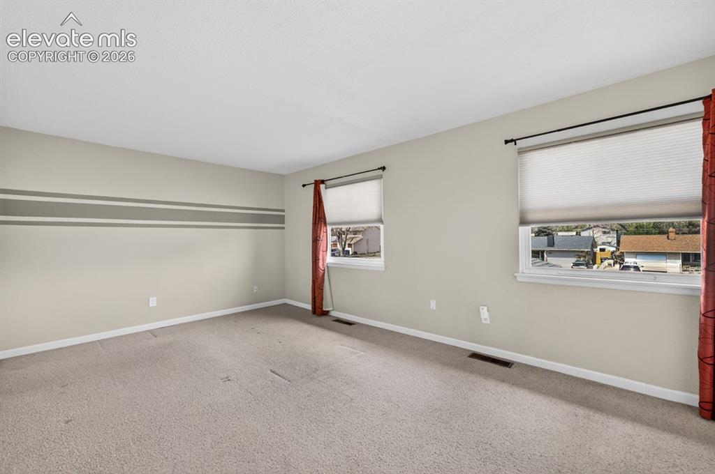 Image 14 of 25: Carpeted room featuring multiple windows with blinds, light-toned walls, an