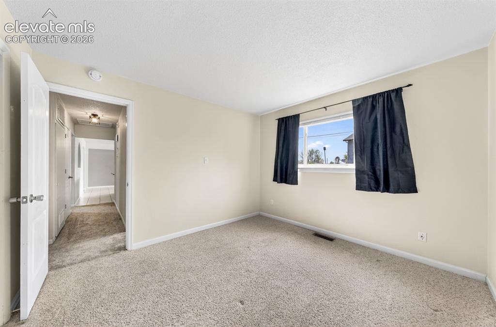 Image 18 of 25: Neutral wall paint, carpeted flooring, and a window with a curtain rod