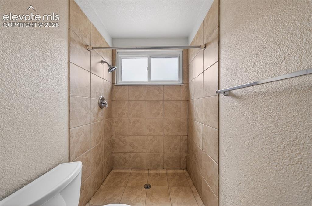 Image 24 of 25: Tiled shower enclosure featuring a window and an integrated shower head wit