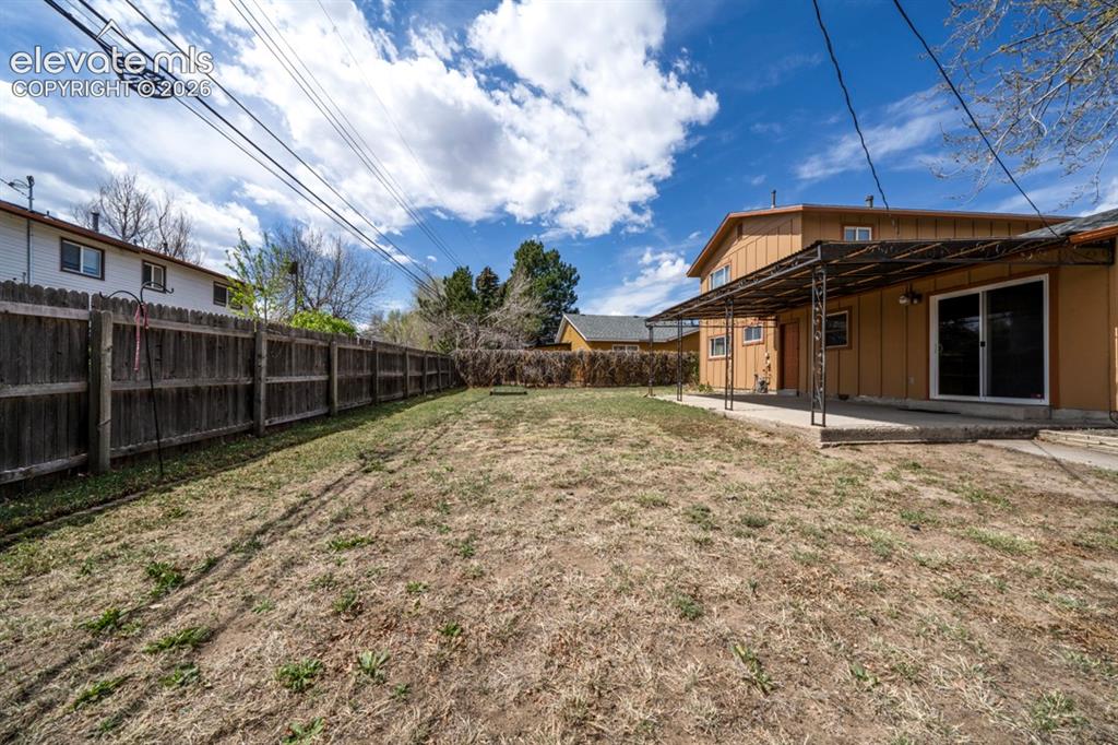 Image 3 of 25: Expansive backyard with a full privacy fence, covered patio, and concrete p
